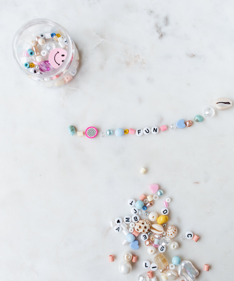 A small DIY box from WALD World containing various beads, along with an assortment of loose beads spelling "FUN" on a light-colored surface, perfect for creating your own Candyman Kit in powder candy Tones.