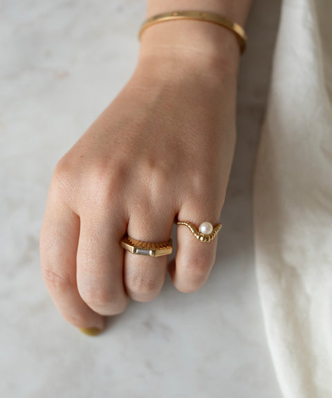 A hand adorned with three WALD Berlin NYC If I Rule The World Rings resting on a marble surface.