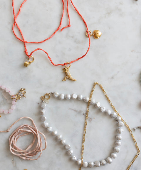 Discover the creative spirit of Esslingen with the DIY Charm Jewelry Workshop by WALD Berlin: an artful array of handcrafted necklaces and pendants—featuring gold charms, pearls, and coral-colored strings—beautifully displayed on a light marble surface.