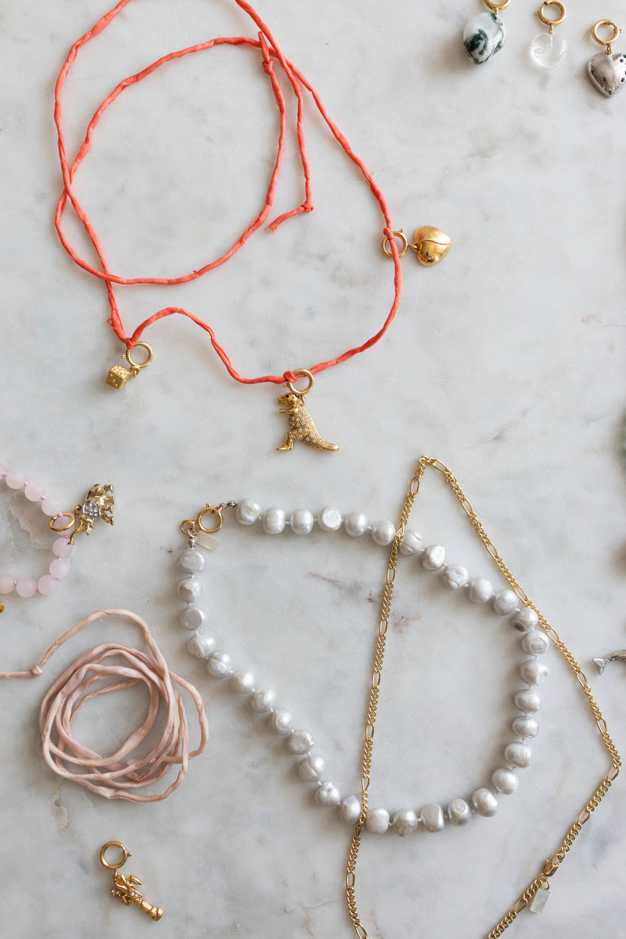 Discover the creative spirit of Esslingen with the DIY Charm Jewelry Workshop by WALD Berlin: an artful array of handcrafted necklaces and pendants—featuring gold charms, pearls, and coral-colored strings—beautifully displayed on a light marble surface.
