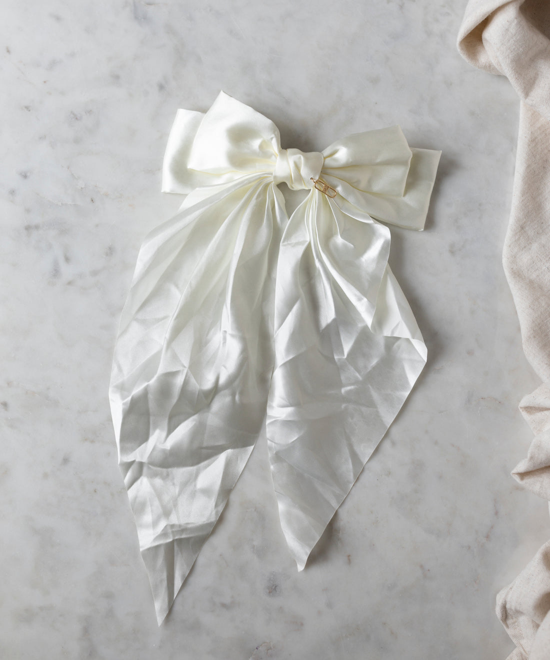 The Happy Holidays Cream Hair Bow by WALD Berlin rests elegantly on a light marble surface, its long, flowing ends cascading downward, making it perfect for festive styling.