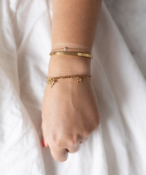 A wrist showcases three 18k gold plated bracelets, including the WALD Berlin SAMPLE SALE Charm Bracelet Z Edition with a delicate charm, elegantly resting on a white fabric background.