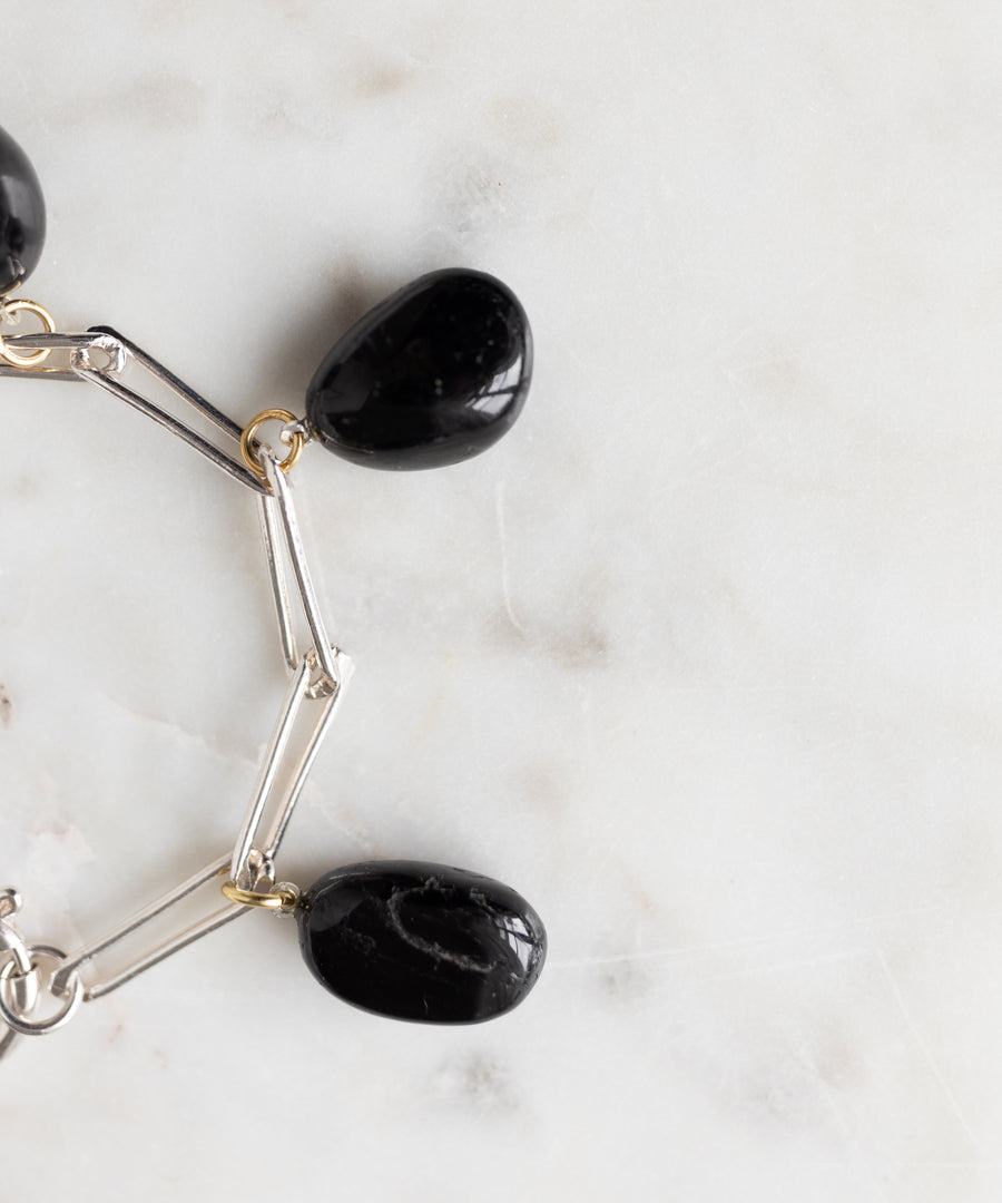 The WALD Berlin Collection Noir Ashley Drop Silver Bracelet, made from recycled silver and featuring three large black stone charms, rests on a white marble surface.