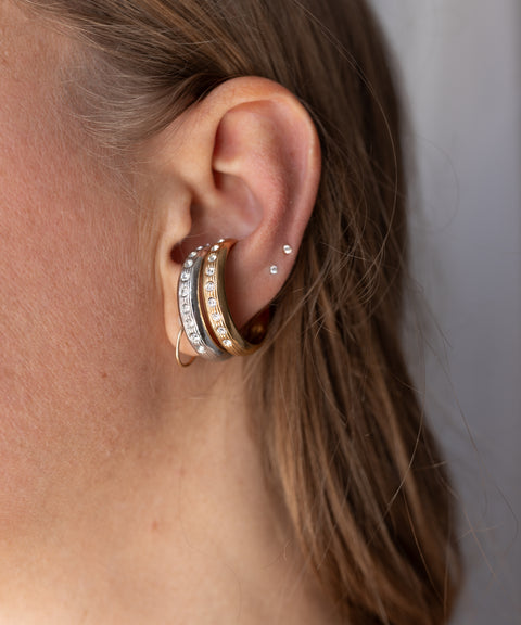 Two stacked silver WALD Berlin Hug Me Earcuff earrings set with small clear Swarovski stones worn on the conch of an ear.