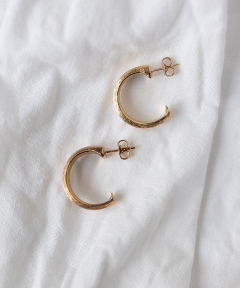 The SAMPLE SALE Pop Classy Hoop Gold earrings by WALD Berlin, featuring 18k gold-plated textured surfaces, are displayed on a white fabric background.