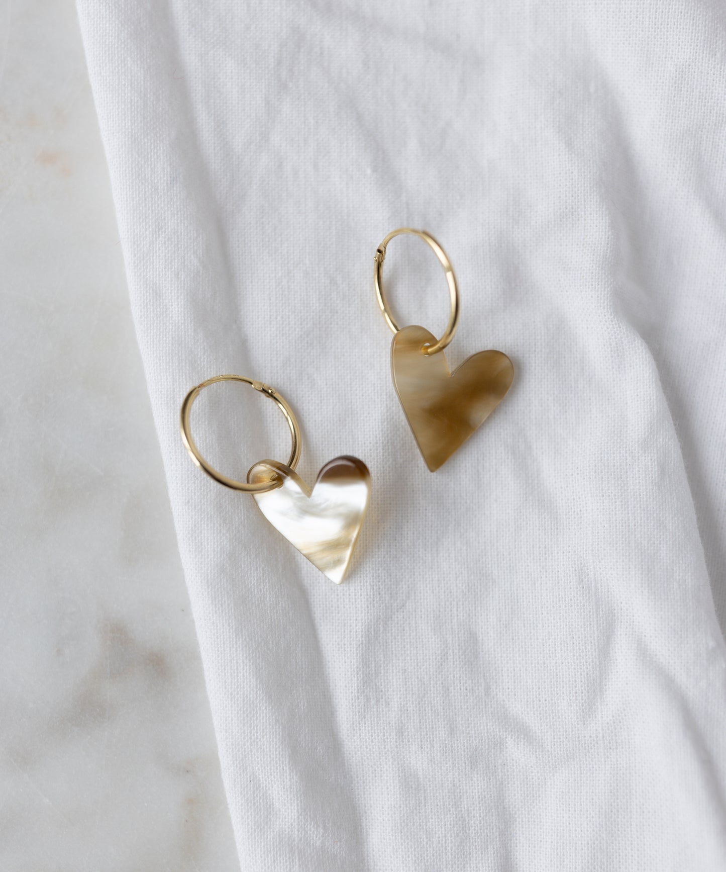 The WALD Berlin Exclusive Heart Black Earrings, featuring recycled gold hoops with heart-shaped pendants, are displayed on a white fabric surface.