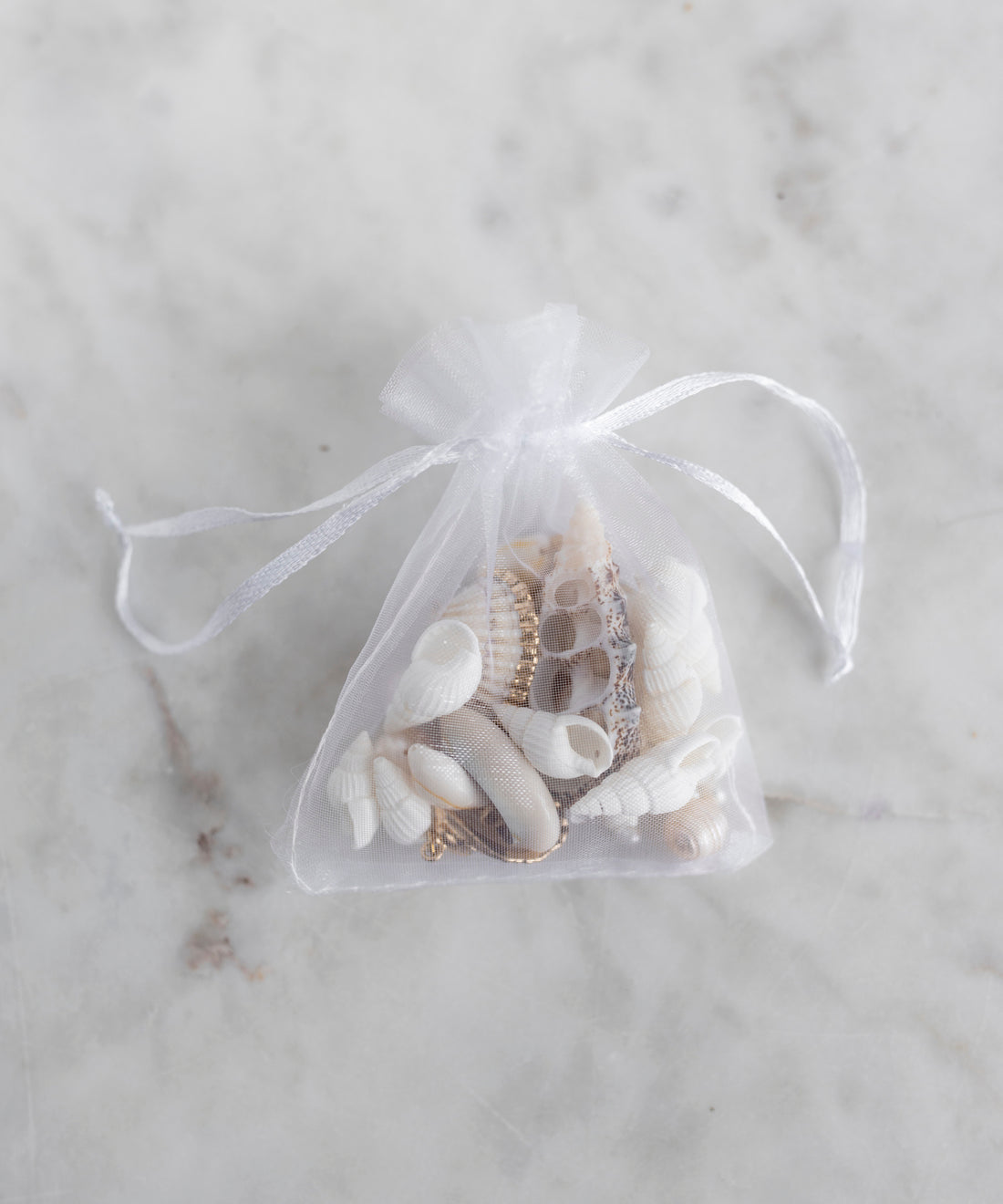 The WALD Berlin Candyman Shell Kit features a small white mesh drawstring bag filled with assorted handpicked seashells, displayed on a light marble surface.
