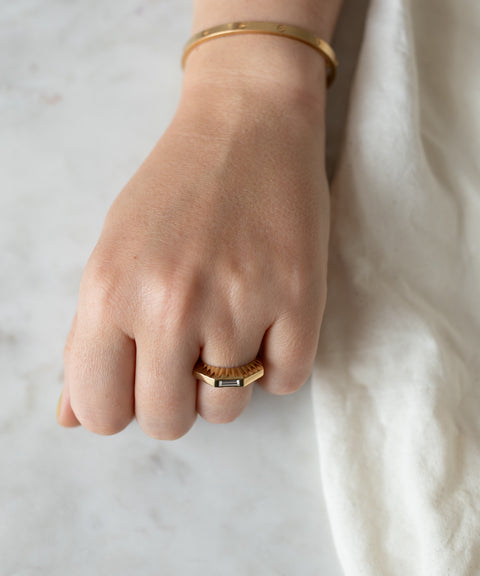 A close-up of a woman's hand resting on a marble surface, wearing a WALD Berlin Shining Star Gold Ring and bracelet.