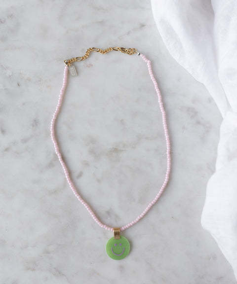 The WALD Berlin Pop Smilie Medallion Green necklace features pink beads, an 18k gold plated clasp, and a green Smilie pendant, adding a playful summer vibe to your look.