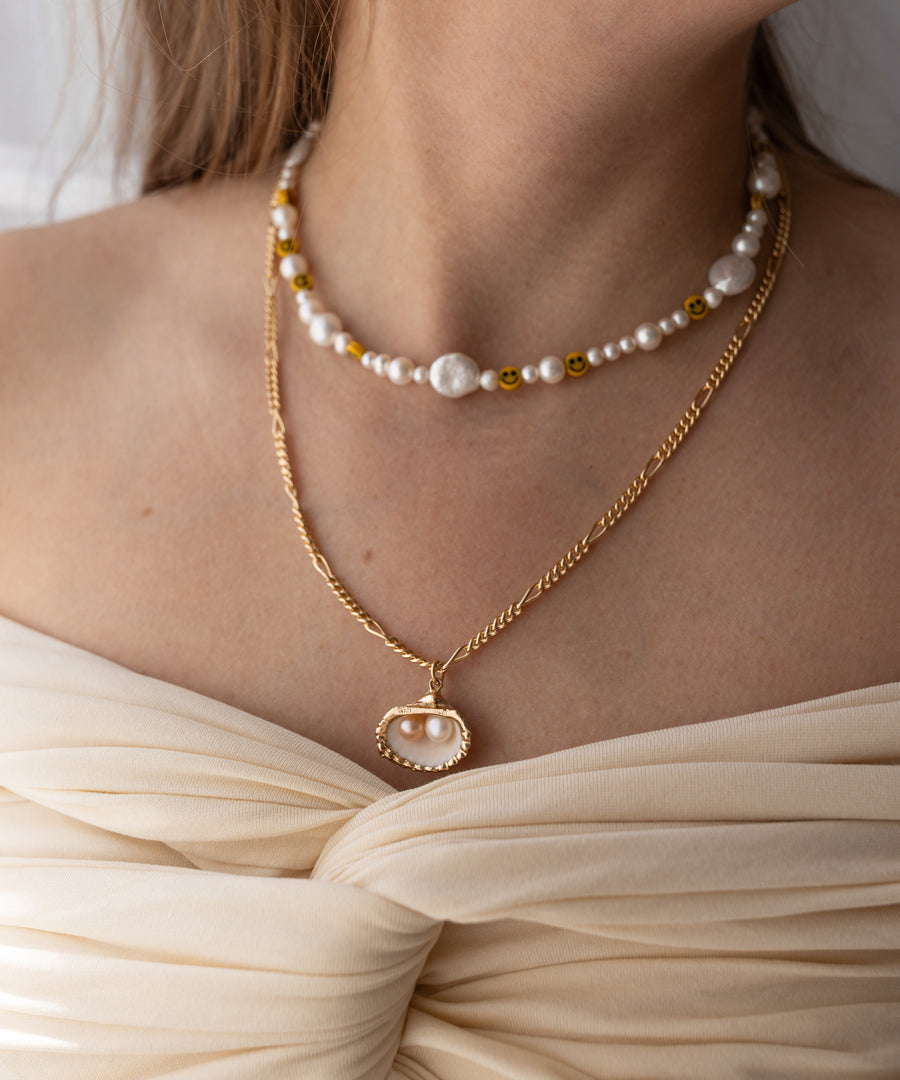 Eine Frau trägt die WALD Berlin Drop It Like It's Hot Shell Necklace mit zwei vergoldeten Halsketten und einem Perlenhalsband und unterstreicht damit ihre Leidenschaft für handgefertigten Schmuck.