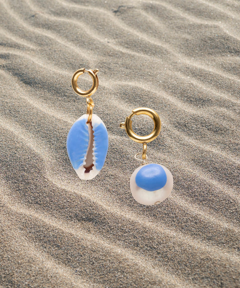 The WALD Berlin SAMPLE SALE Beach Babe Charms feature two gold hoop earrings with blue and white shell pendants and sweetwater pearl accents, styled on rippled sand.
