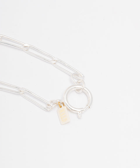 The SAMPLE SALE Ashley Bracelet Silver by WALD Berlin, featuring elongated silver-plated links, a circular clasp, and a small rectangular gold tag, is displayed on a white background.