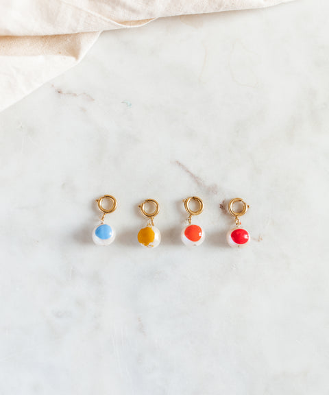 Four gold-plated brass hoop earrings from WALD Berlin's SAMPLE SALE Beach Babe Charms feature round blue, yellow, orange, and red pendants arranged on white marble for a playful, beach-inspired look.