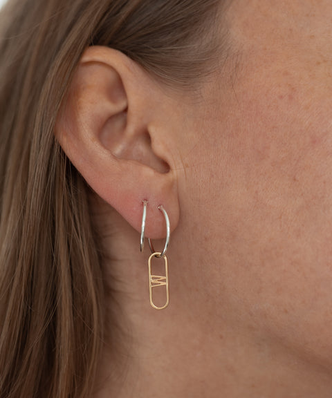 Close-up of a person's ear wearing the SAMPLE SALE NYC Cream Earrings by WALD Berlin, featuring hand-made sterling silver hoops each adorned with a gold geometric charm.