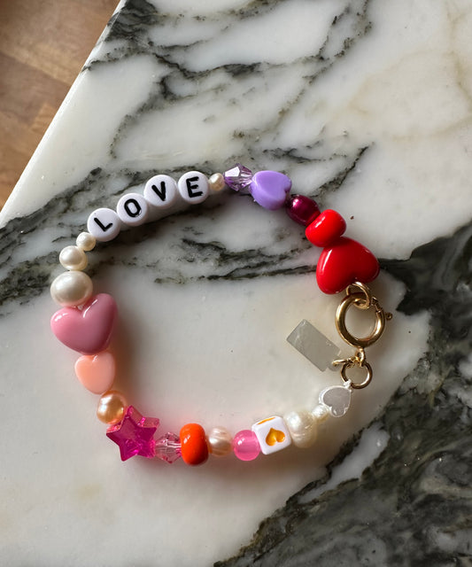 Discover the WALD Berlin Personalized Bracelet, featuring vibrant beaded hearts, stars, sweetwater pearls, and letter beads spelling “LOVE”—displayed on a marble surface. This charming accessory makes an ideal custom name or personalized bracelet for someone special.