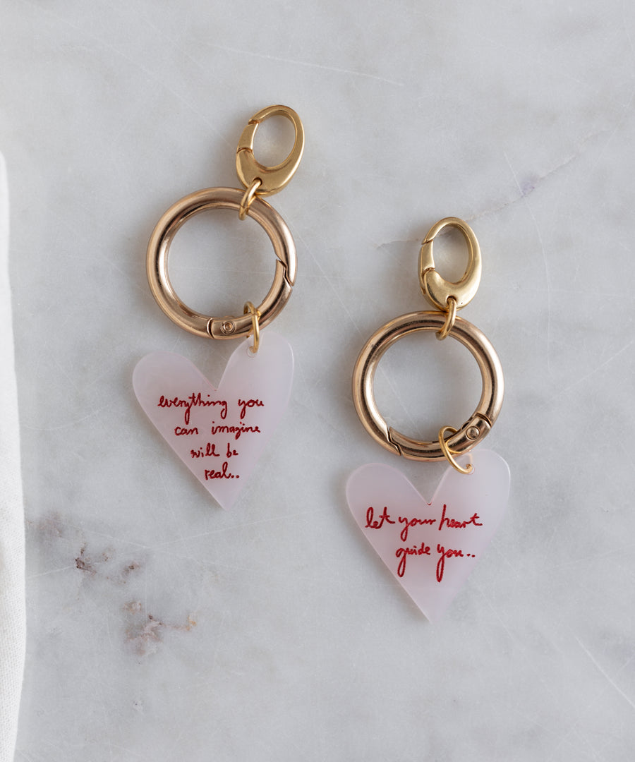 Two gold WALD Berlin key chains from the SAMPLE SALE, crafted in Germany from brass and bio polyester, each with a translucent heart pendant—one says "everything you can imagine will be real," the other, "let your heart guide you.