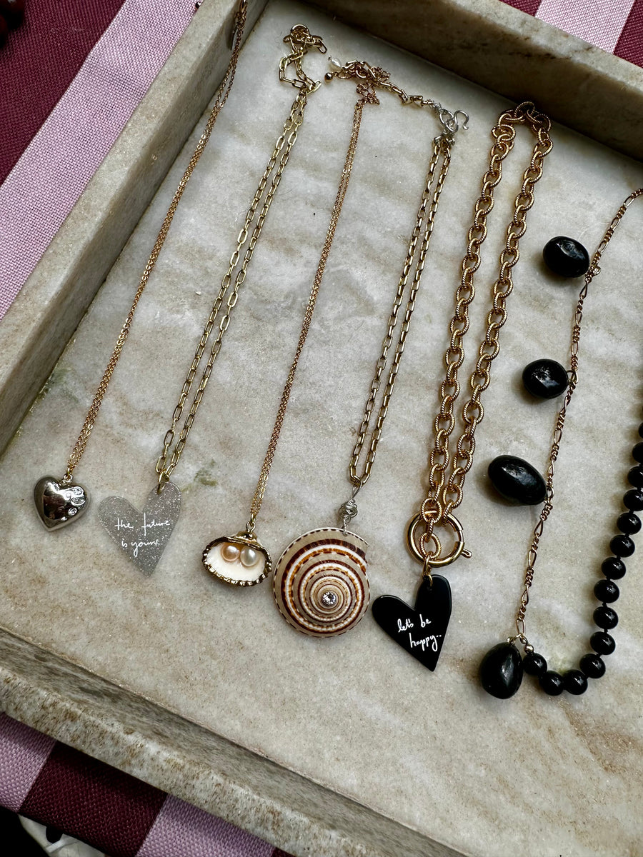 Eine Überraschungspackung von WALD Berlin mit fünf Halsketten mit Herzanhängern, einem Muschelanhänger, einem runden Anhänger und einer schwarzen Perlenkette – ideal für Liebhaber von Designerschmuck.