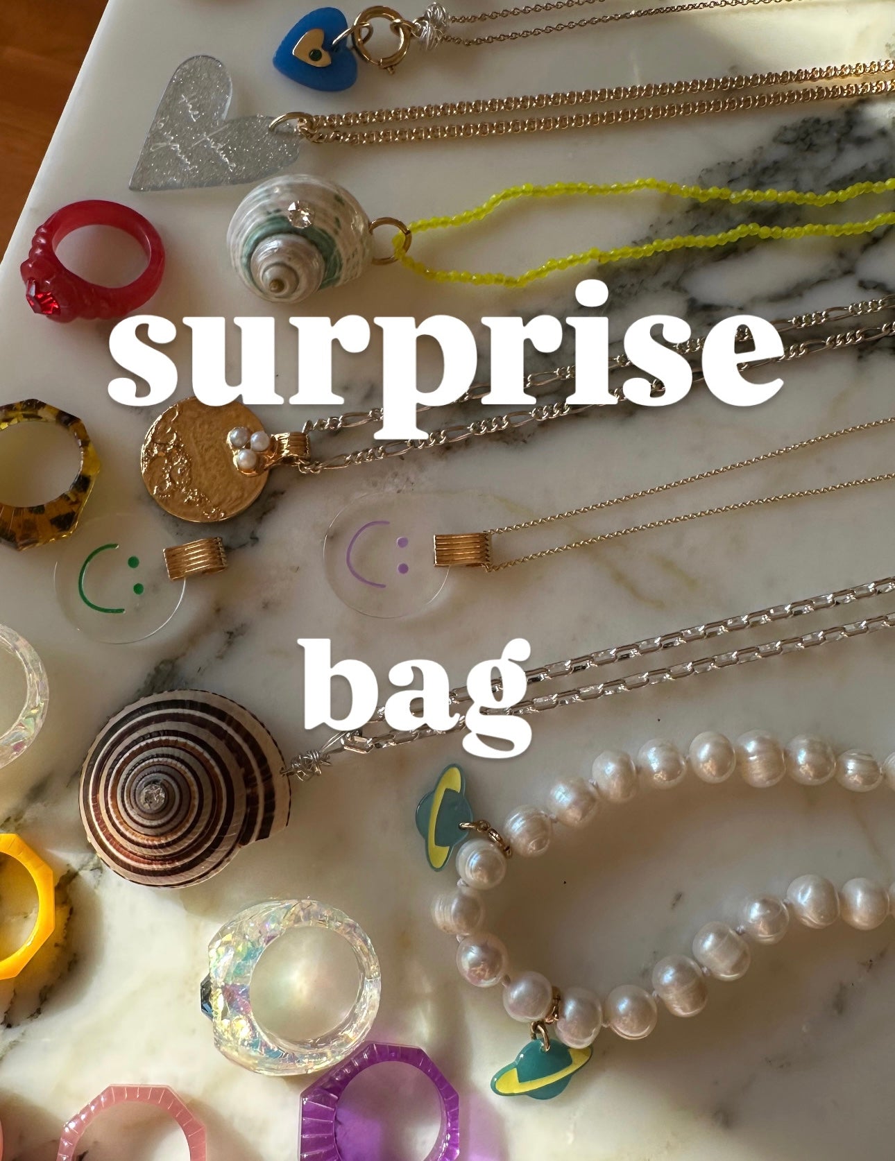 Various WALD Berlin jewelry and accessories are stylishly arranged on a marble surface with the text "surprise WALD Berlin Bag" overlayed, showcasing pieces inspired by designer Dana Roski.