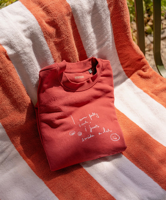A limited edition PRETTY COOL jumper by WALD Berlin, featuring white handwriting, rests on a striped orange and white towel draped over a chair, crafted from bio cotton for ultimate comfort.