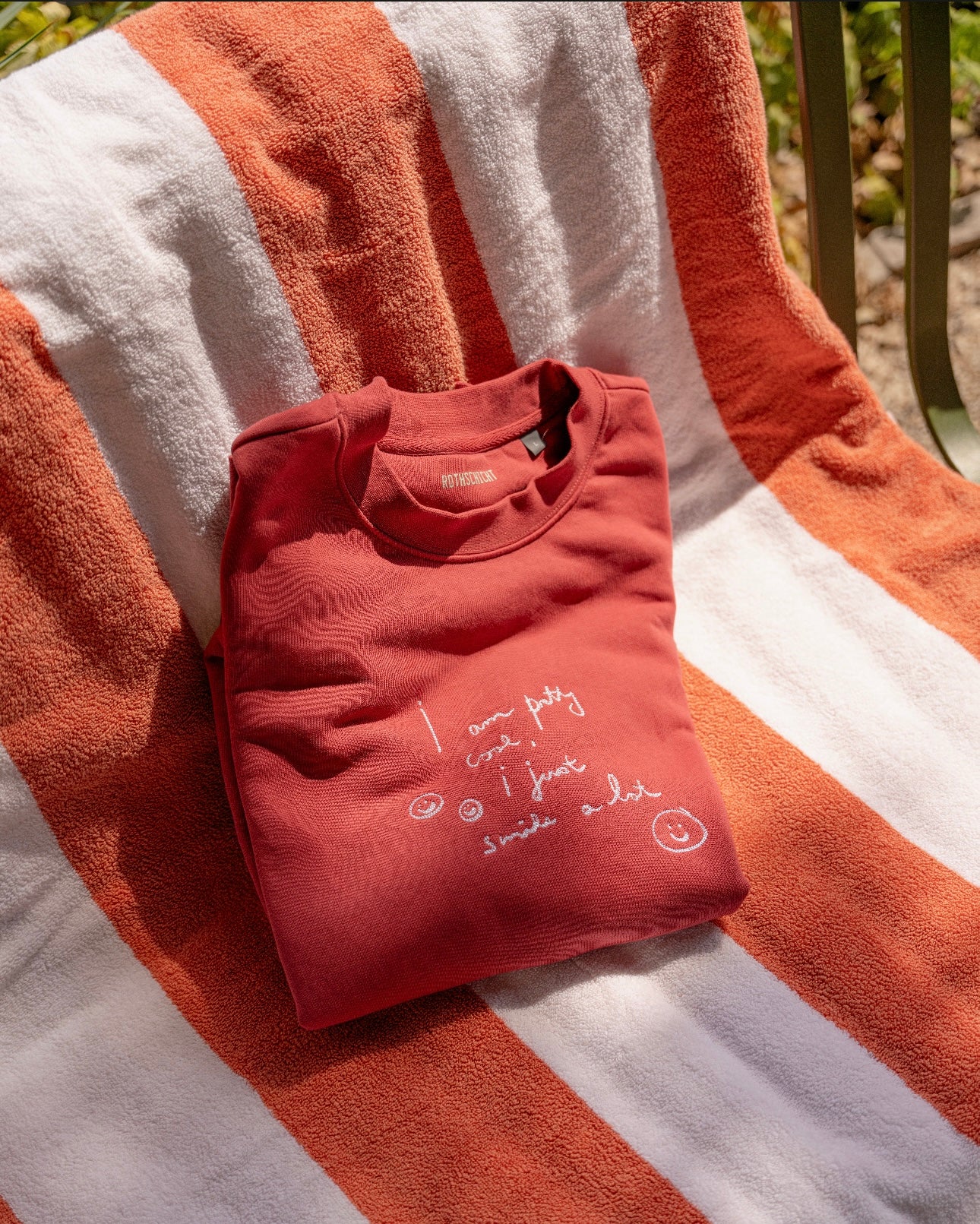 A limited edition PRETTY COOL jumper by WALD Berlin, featuring white handwriting, rests on a striped orange and white towel draped over a chair, crafted from bio cotton for ultimate comfort.
