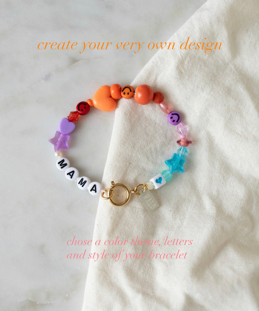 Introducing the Personalized Bracelet from WALD Berlin, featuring vibrant, colorful beads and “MAMA” letter beads elegantly displayed on a white cloth. Add your own custom design text above and below the bracelet to make this accessory uniquely yours—create the perfect custom name bracelet for a truly personal touch.