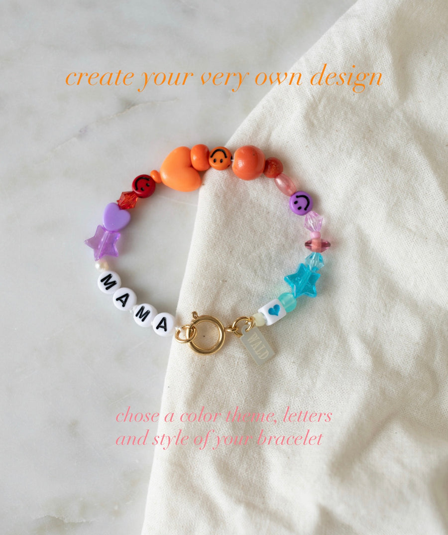 Introducing the Personalized Bracelet from WALD Berlin, featuring vibrant, colorful beads and “MAMA” letter beads elegantly displayed on a white cloth. Add your own custom design text above and below the bracelet to make this accessory uniquely yours—create the perfect custom name bracelet for a truly personal touch.
