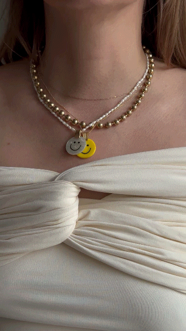 A person wearing a white off-shoulder top and WALD Berlin's Smilie Dude Medaillon Pearl Necklace with spring colors and pearl beads.