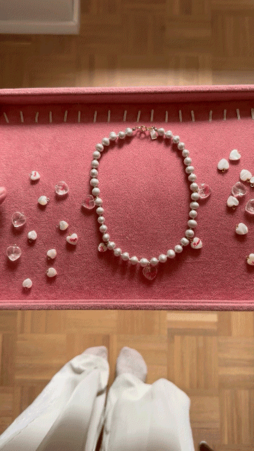 The Limited HI MAMA Pearl Necklace by WALD Berlin, featuring real sweet water pearls and pink heart-shaped pendants, is displayed on a pink tray with loose heart beads nearby—perfect for Mother’s Day.