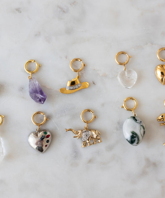 Neun Anhänger für Goldschmuck – darunter Formen wie Herzen, Steine, ein Cowboyhut und ein Elefant – sind auf Marmor ausgestellt und dienen als perfekte Inspiration für Ihren nächsten DIY-Schmuck-Workshop x MINI im KaDeWe Berlin von WALD Berlin oder Ihr eigenes Charm-DIY-Projekt.