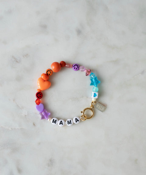 WALD Berlin’s personalized bracelet displayed on a marble surface, featuring colorful beads in star and heart shapes, white letter beads spelling “MAMA,” a small gold clasp, and an attached “WALD” tag.