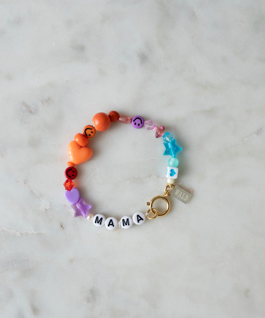 WALD Berlin’s personalized bracelet displayed on a marble surface, featuring colorful beads in star and heart shapes, white letter beads spelling “MAMA,” a small gold clasp, and an attached “WALD” tag.