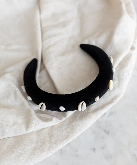 The SAMPLE SALE Simone de Beauvoir Black Headband by WALD Berlin—a handmade black velvet crescent headband adorned with white cowrie shells—is a unique piece from the limited Wiesn collection, ideal as an Oktoberfest accessory.