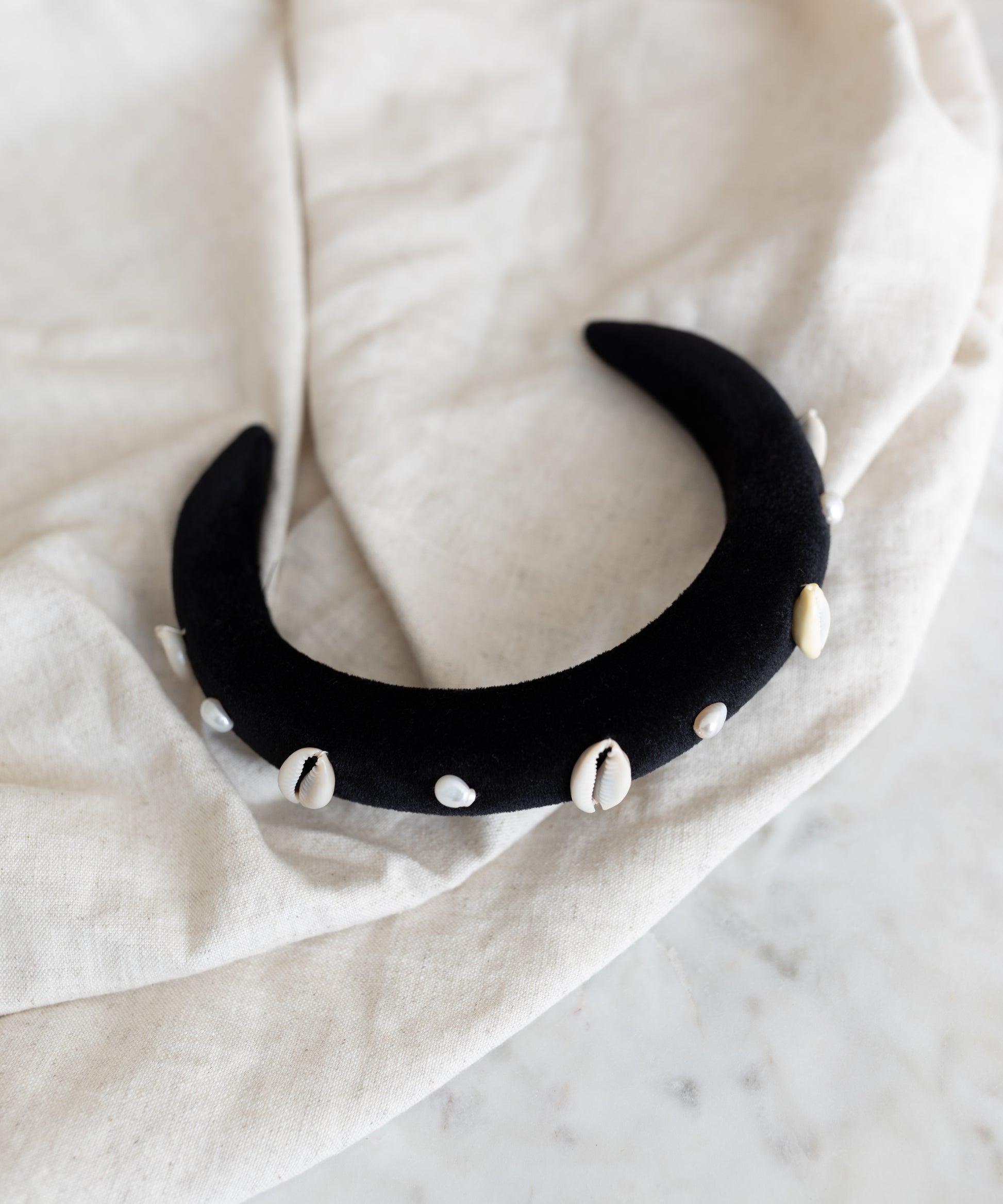 The SAMPLE SALE Simone de Beauvoir Black Headband by WALD Berlin—a handmade black velvet crescent headband adorned with white cowrie shells—is a unique piece from the limited Wiesn collection, ideal as an Oktoberfest accessory.
