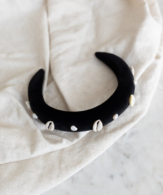 The SAMPLE SALE Simone de Beauvoir Black Headband by WALD Berlin—a handmade black velvet crescent headband adorned with white cowrie shells—is a unique piece from the limited Wiesn collection, ideal as an Oktoberfest accessory.