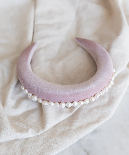 The SAMPLES SALE Lady Di Headband Rose by WALD Berlin, a wide pale pink velvet band adorned with white pearls, rests on a light beige fabric—highlighting the elegance of this handmade German accessory.