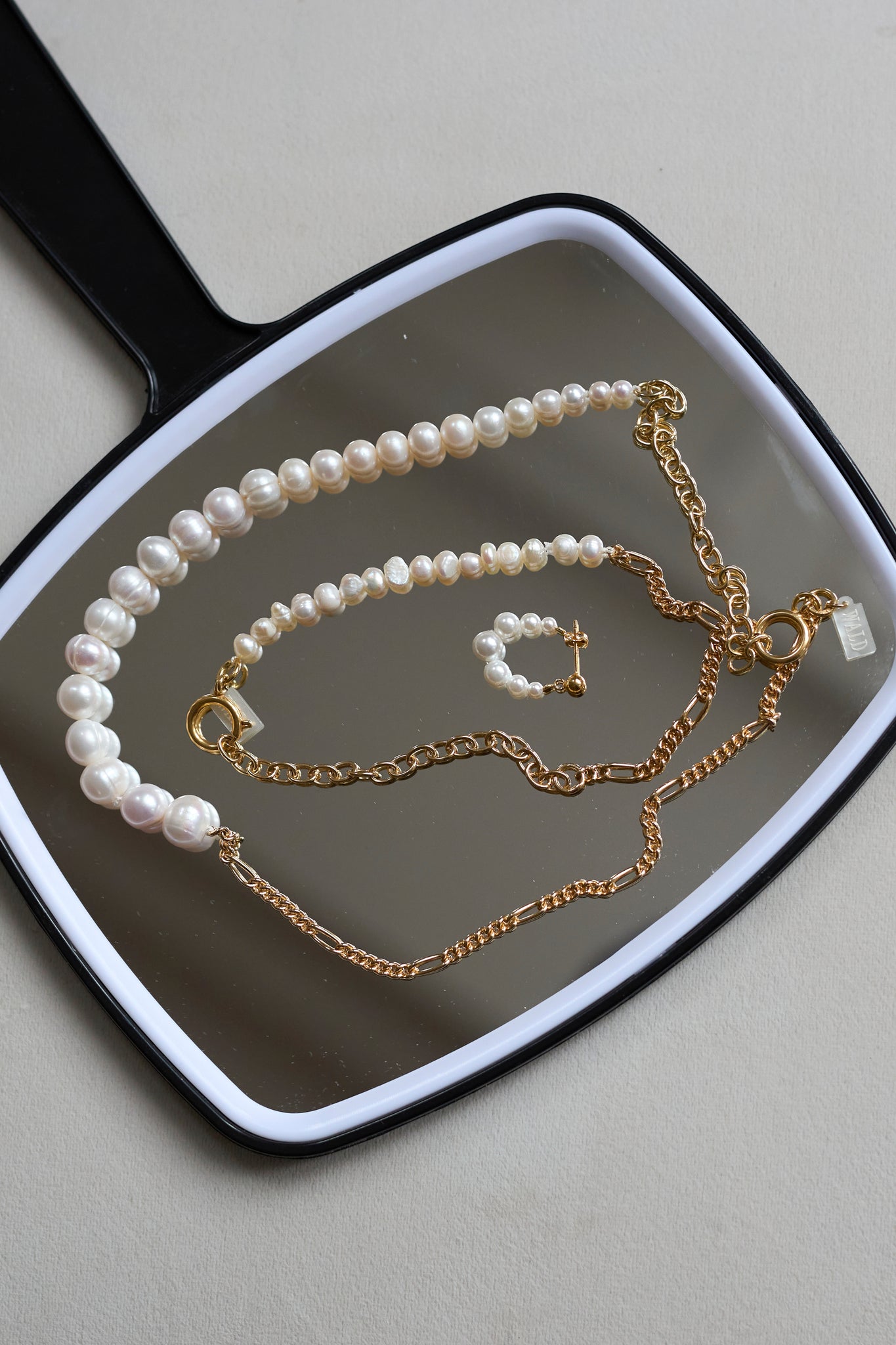 The WALD Berlin Pas De Deux Bracelet / Anklet is elegantly displayed on a black hand mirror, highlighting the brand’s exquisite handmade jewelry design.