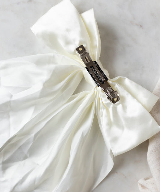 The Happy Holidays Cream Hair Bow by WALD Berlin is elegantly secured with a metallic clip on the marble surface, adding a festive touch.