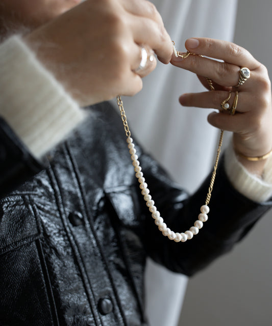 A person holding the Pas De Deux Necklace by WALD Berlin, adorned with rings and wearing a black leather jacket.