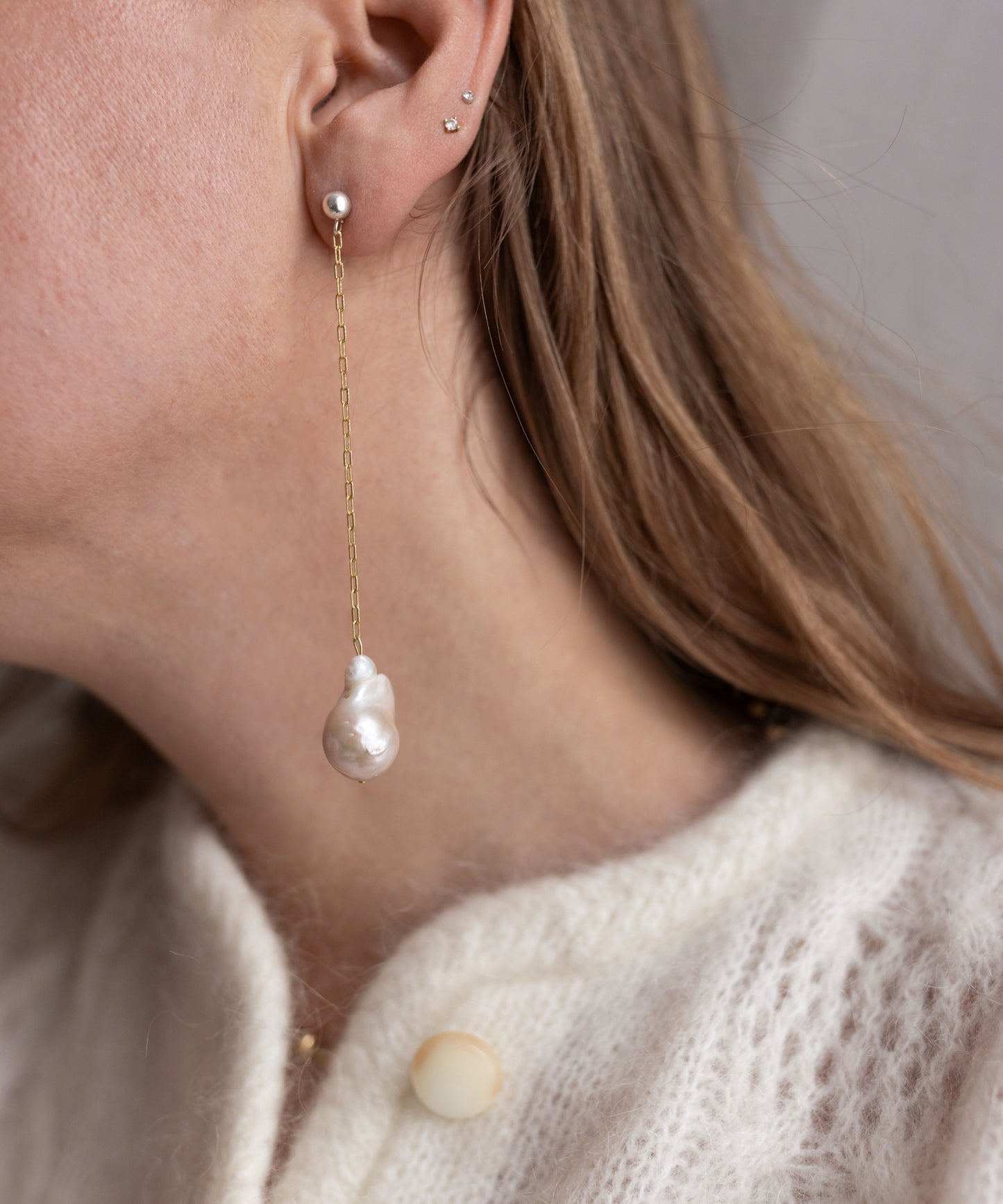 A person wearing WALD Berlin's Happy Holidays Pearl Drop Earrings and a cream knit sweater.