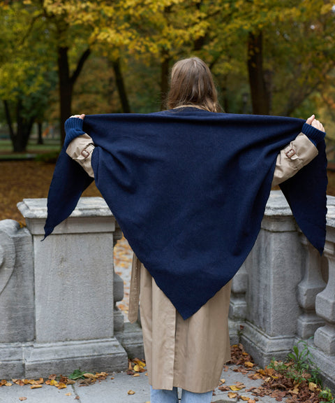 Eine Person, die von hinten zu sehen ist, trägt einen Trenchcoat und hält einen großen, marineblauen „WALD Berlin x Helena Harfst Homeland“-Schal offen hinter dem Rücken.