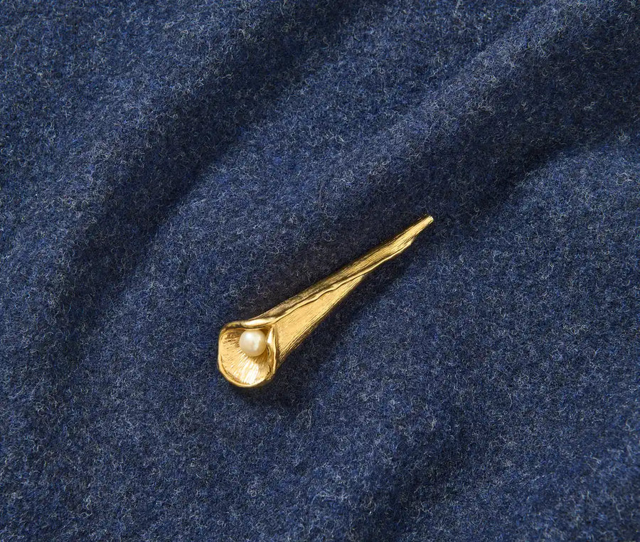 Goldfarbene Calla-Lilien-Brosche mit einer kleinen weißen Perle, befestigt an einem strukturierten blauen „Homeland“-Schal von WALD Berlin x Helena Harfst (Vorbestellung).