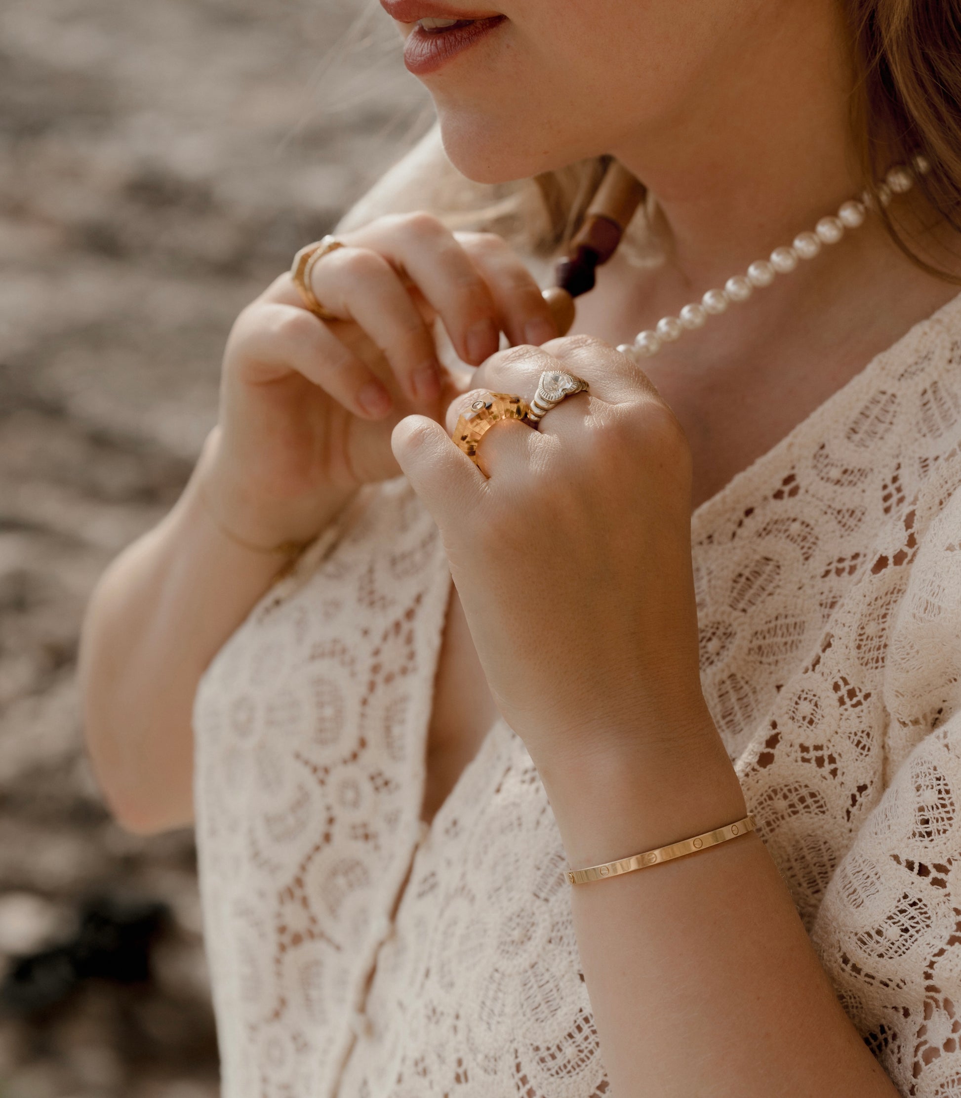 A woman wearing a lace blouse and an amber color bracelet is adjusting a pearl necklace. She has rings on her fingers, including the Isla Bonita Shining Star ring by WALD Berlin.