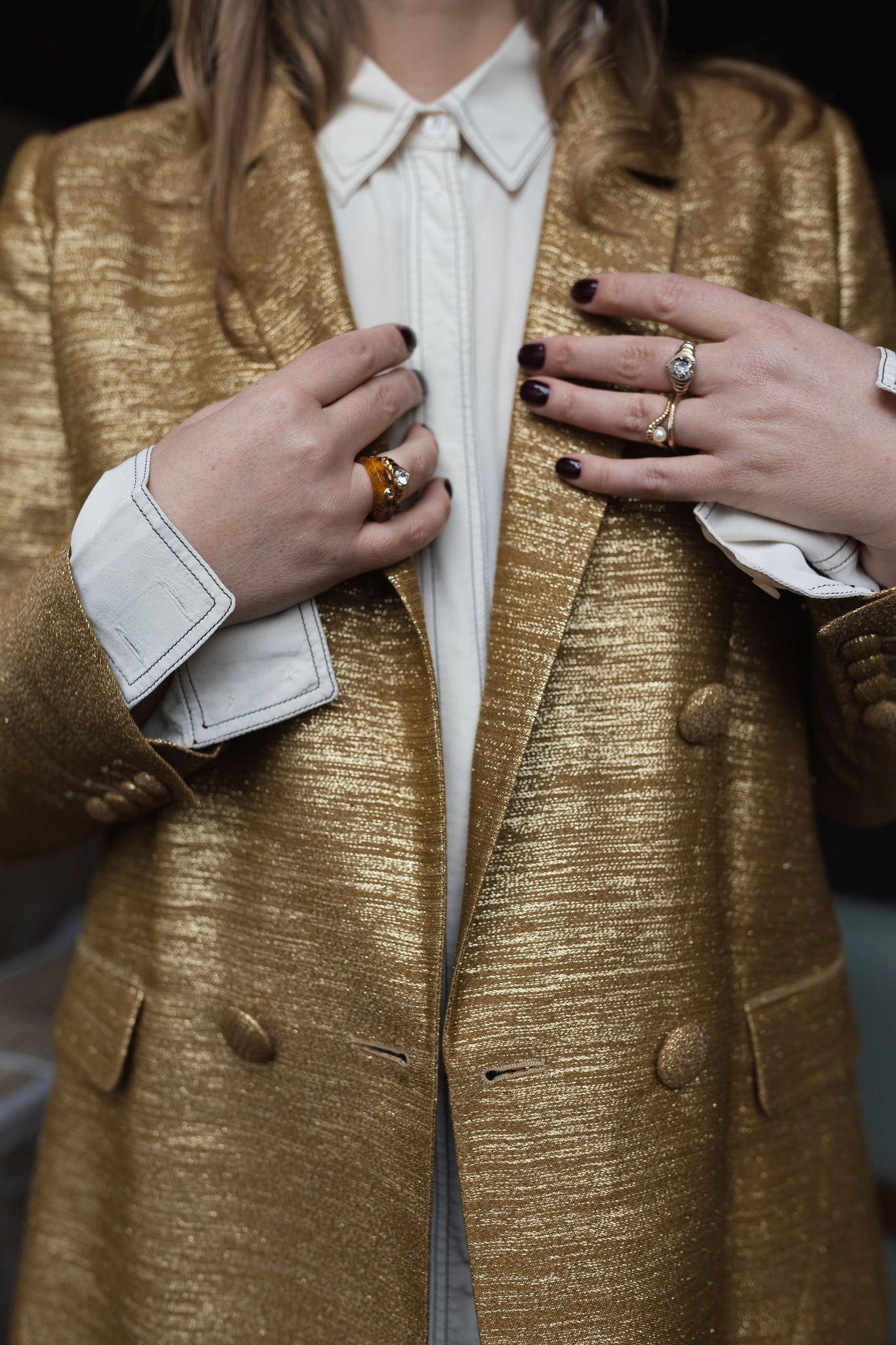 A person in a shiny gold blazer made from bio polyester, over a white shirt, showcases Isla Bonita shining star rings by WALD Berlin adorned with Swarovski stones and wears dark nail polish.