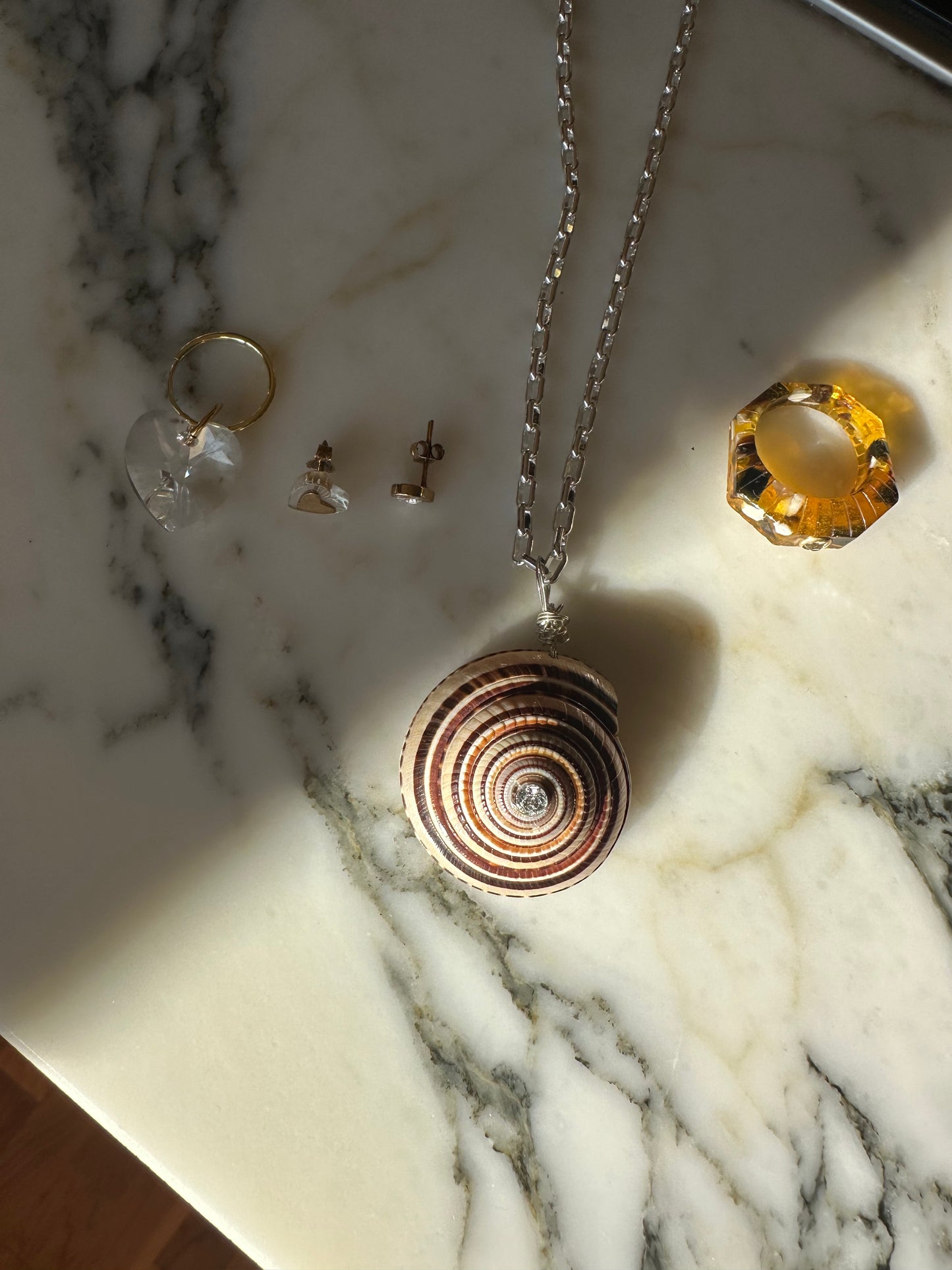 A surprise WALD Berlin Bag, with a spiral shell necklace on a silver chain, two rings, and three earrings, is elegantly arranged on a marble surface.