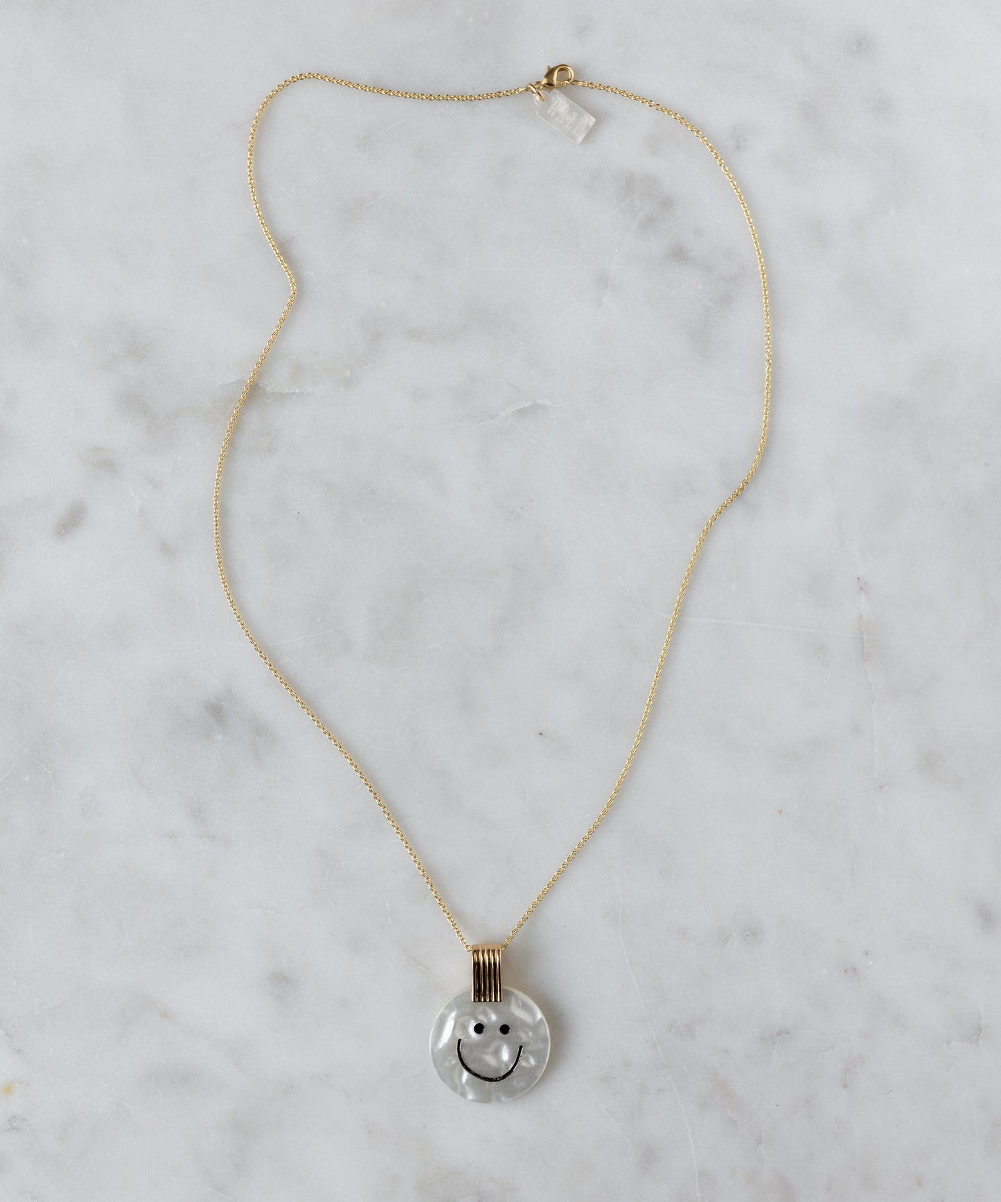 The WALD Berlin Smilie Dude Medaillon Pearl Necklace features an 18k gold-plated chain and round pendant with a smiley face on a white marbled background, adding cheerful spring colors to any outfit.