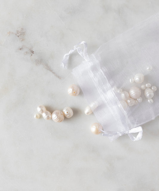 A small open drawstring bag on a marble surface with various sizes and shapes of unique pearls spilled out, perfect for your DIY collection. Introducing the Sweet Water Pearls Kit by WALD World.
