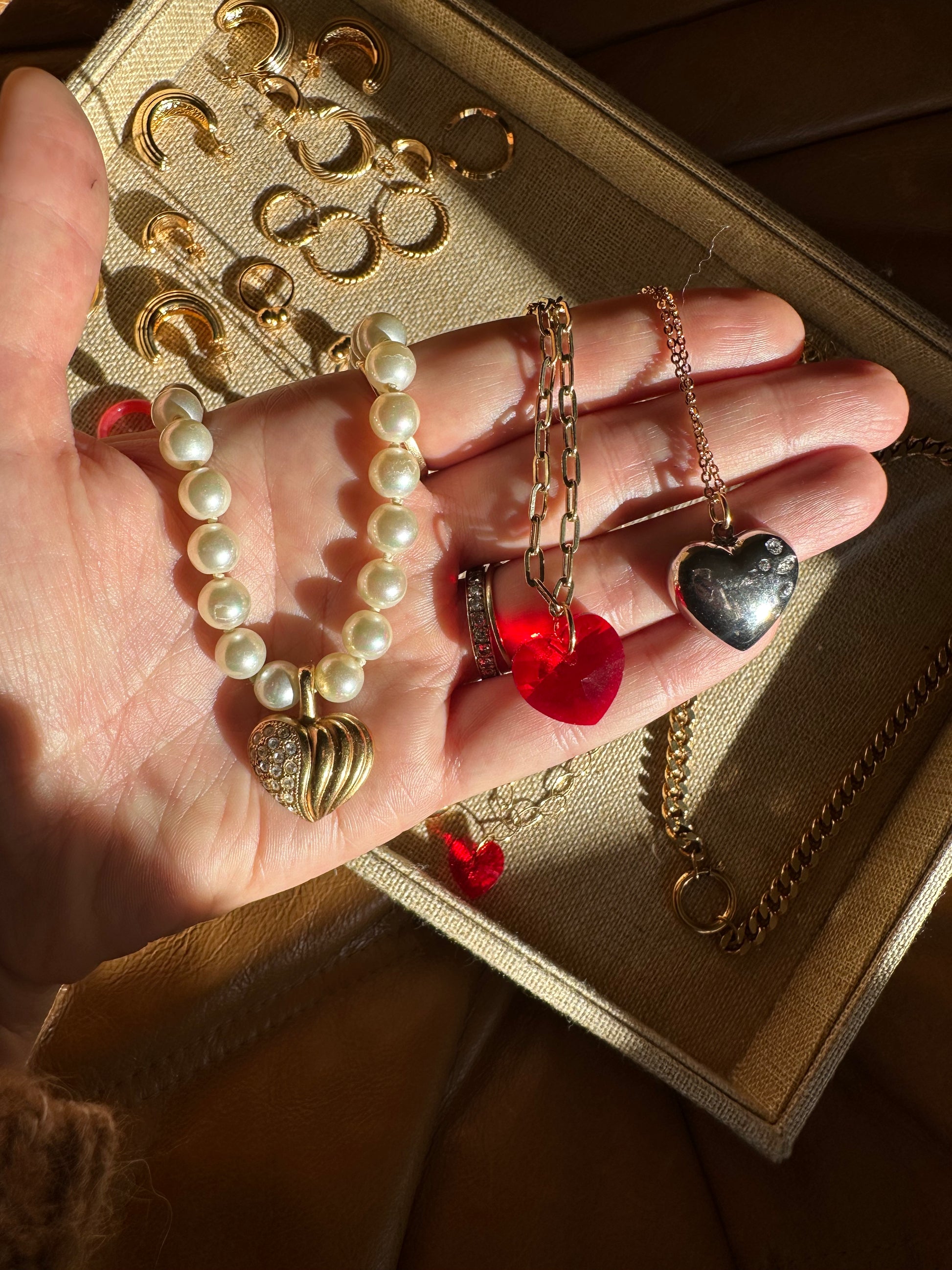 A hand displays a pearl bracelet with gold charms, earrings, a red heart pendant, and a silver ring. More jewelry rests in a beige tray beside the chic surprise WALD Berlin Bag by WALD Berlin.