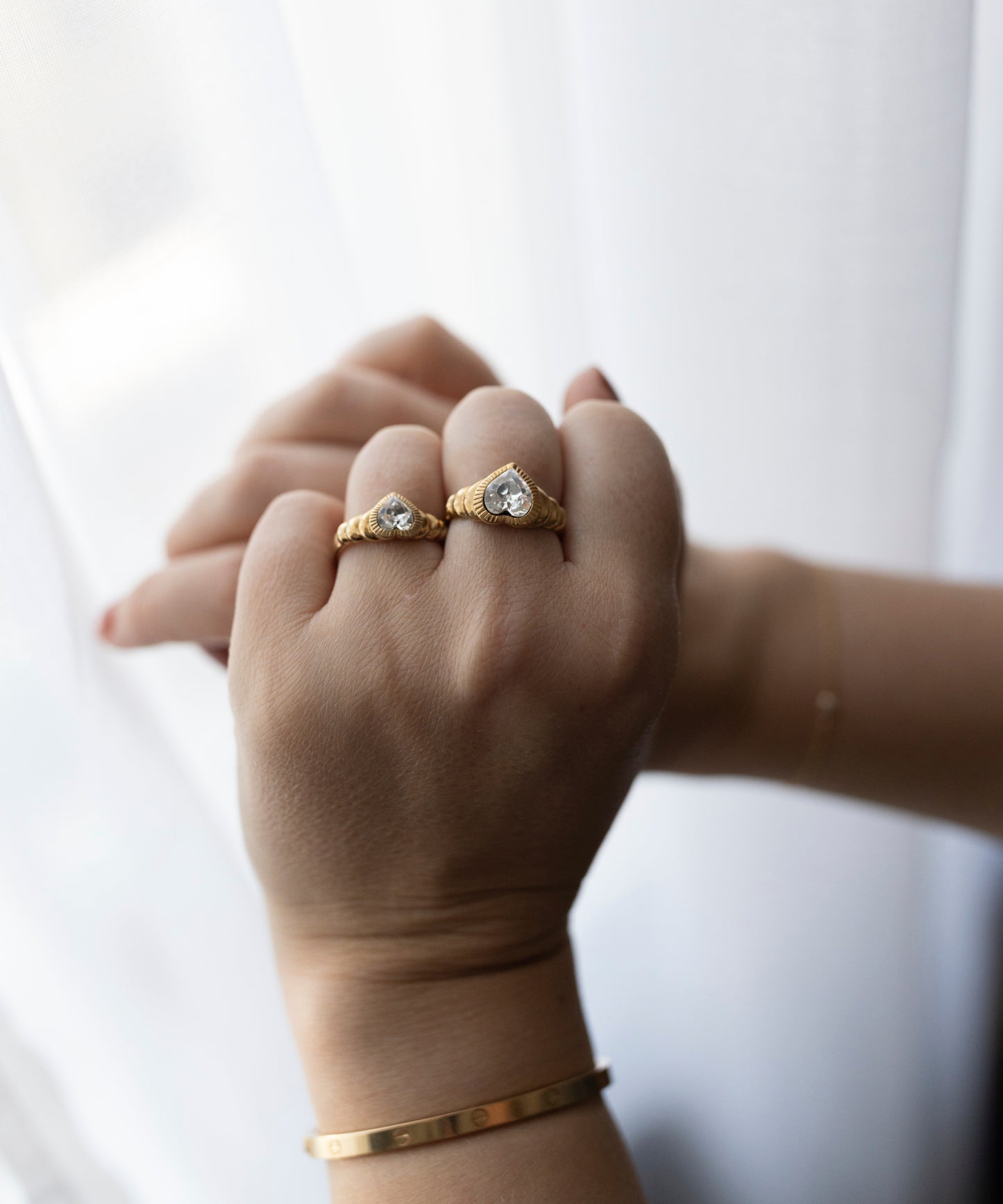 A hand adorned with two Be My Lover Ring Mini rings by WALD Berlin, one featuring a Swarovski stone, in front of a sheer white curtain.