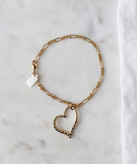 The WALD Berlin Valentines Day special sketch heart bracelet features a heart-shaped pendant with sparkling Swarovski stones, shown on a white marble surface beside a white cloth.