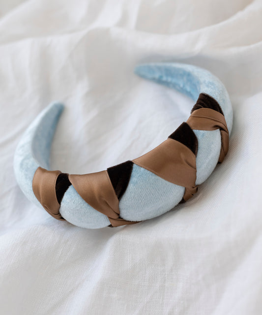 The SAMPLE SALE Headband Knot Light Blue by WALD Berlin is handmade in Germany, featuring a light blue velvety base with a brown and black satin braided design, displayed on a white fabric surface.
